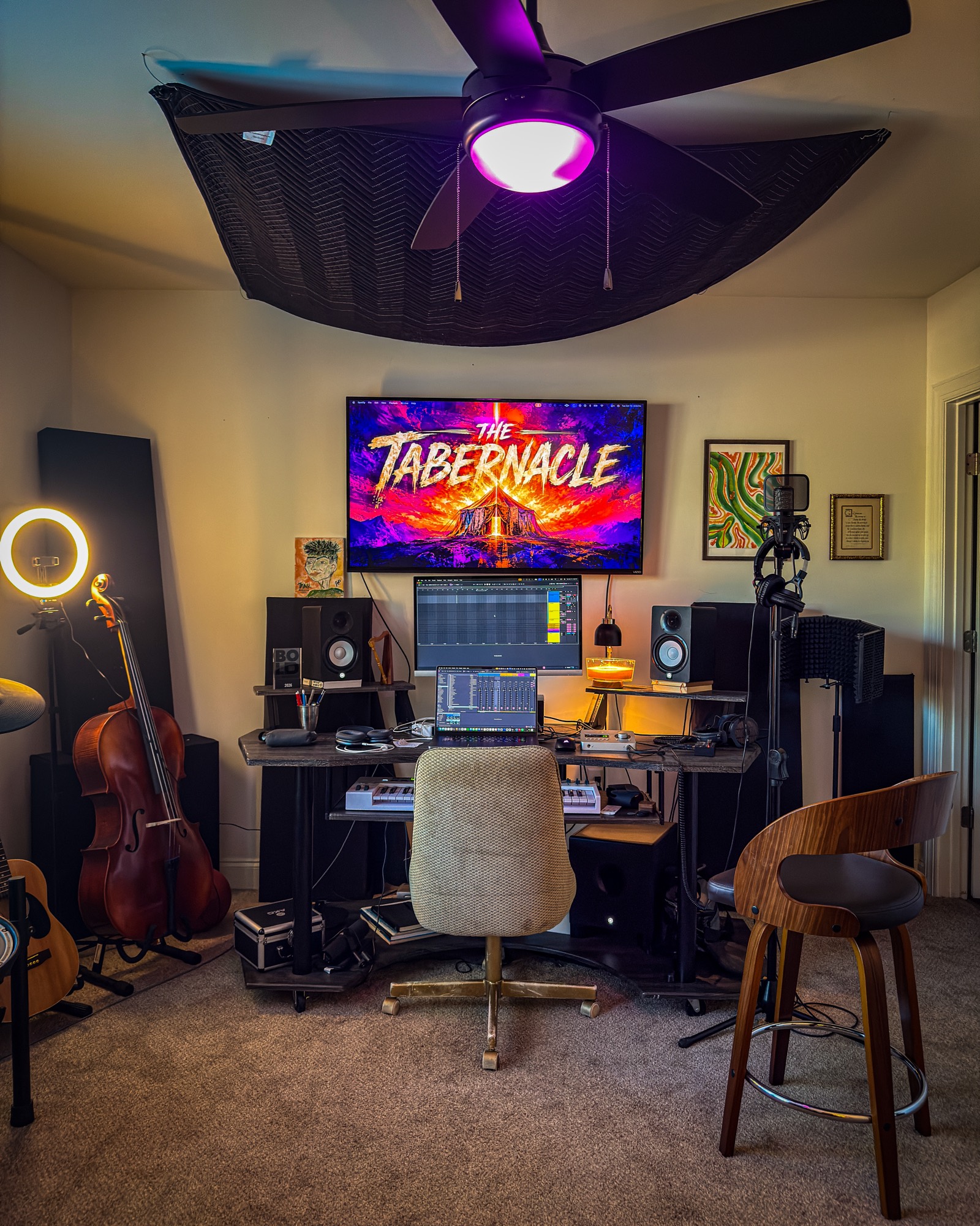 The studio desk under a ceiling cloud, with monitors, a cello, and The Tabernacle on the screen.